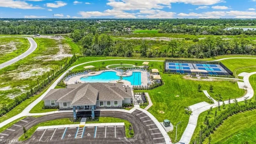 Community clubhouse with an expansive swimming pool, adjacent tennis courts, walking paths, and surrounding green spaces