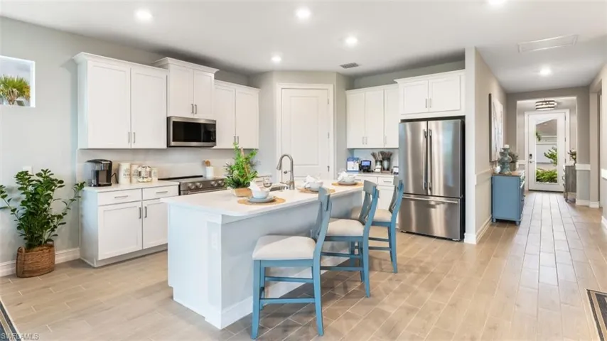 Kitchen featuring white shaker-style cabinetry, stainless steel appliances, a center island with seating, and light wood-finish flooring