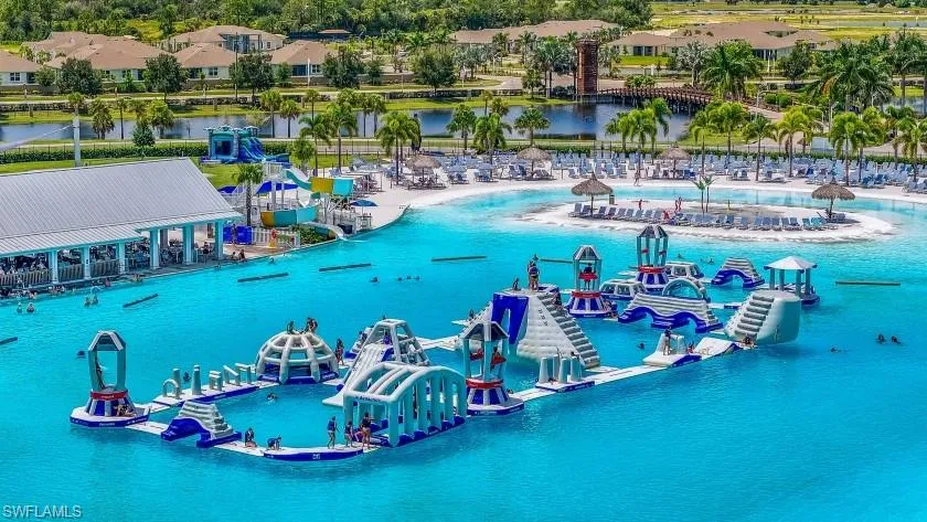 Expansive lagoon with a water obstacle course, sandy beach area, waterslides, and a shaded open-air structure