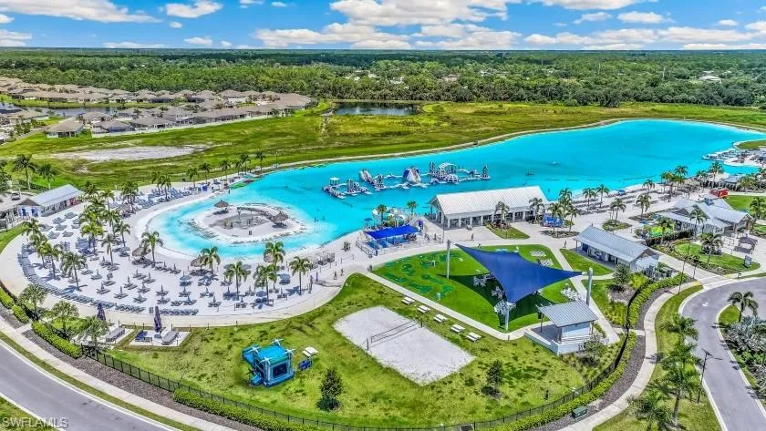 Expansive turquoise lagoon with a sandy beach area, multiple recreational buildings, a shaded lawn, and a sand volleyball court