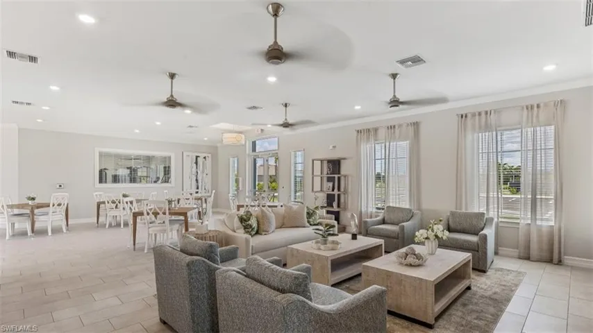 Expansive covered patio with paver flooring, multiple ceiling fans, and direct access to a large swimming pool area with surrounding landscaping
