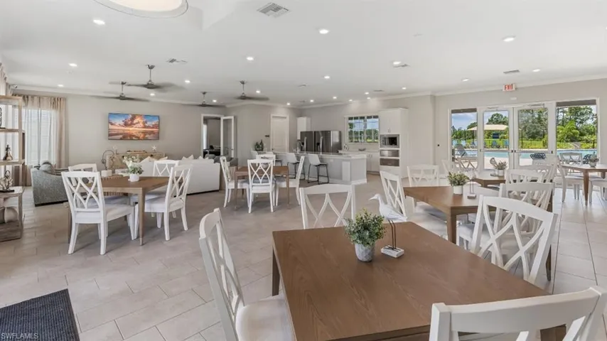 Spacious common area featuring light-toned tile flooring, multiple ceiling fans, and an abundance of natural light from large windows and glass-paneled double doors