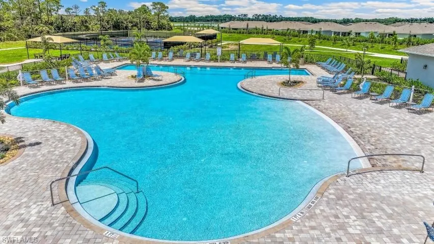 Expansive swimming pool with integrated steps, surrounded by paver decking, multiple shade structures, and lush landscaping