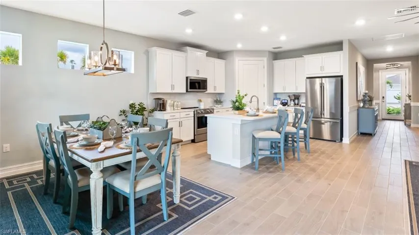 Open-concept layout featuring wood-finish flooring, white cabinetry, stainless steel appliances, and a kitchen island with seating