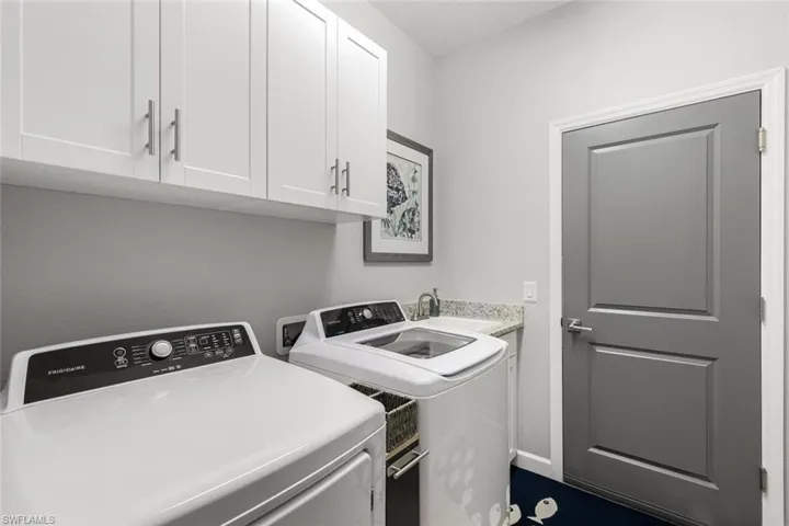 Clothes washing area featuring sink, washing machine and clothes dryer, and cabinets