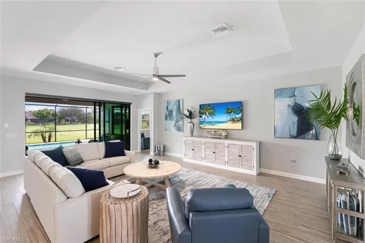 Living room with wood-type flooring, a tray ceiling, and ceiling fan