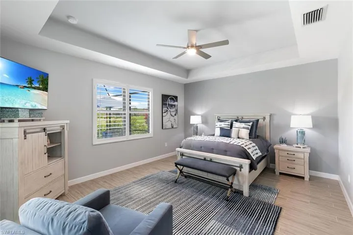 Bedroom featuring light wood-type flooring, a tray ceiling, and ceiling fan