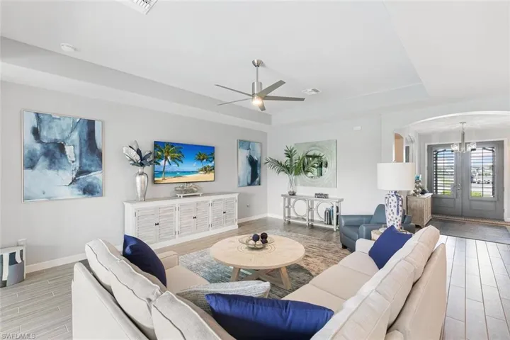 Living room with ceiling fan with notable chandelier, a tray ceiling, and light hardwood / wood-style flooring