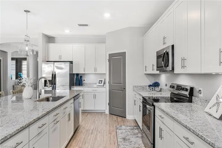 Kitchen with hanging light fixtures, sink, white cabinetry, appliances with stainless steel finishes, and light wood-type flooring