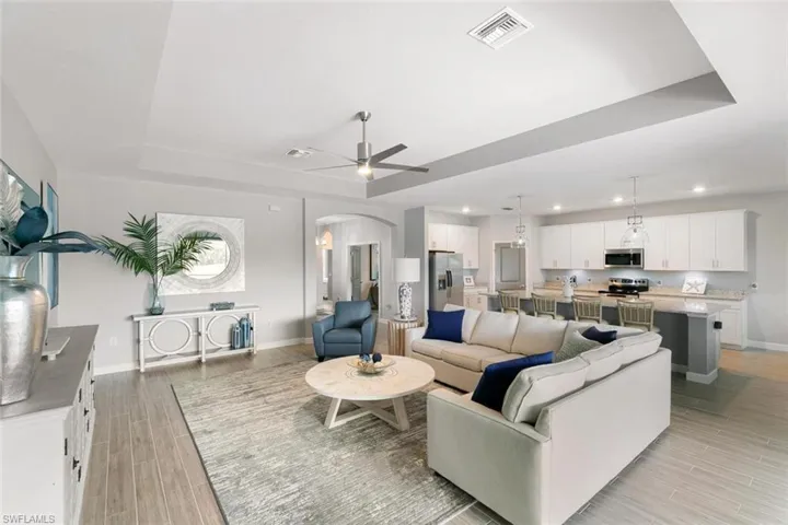 Living room with light wood-type flooring, a tray ceiling, and ceiling fan