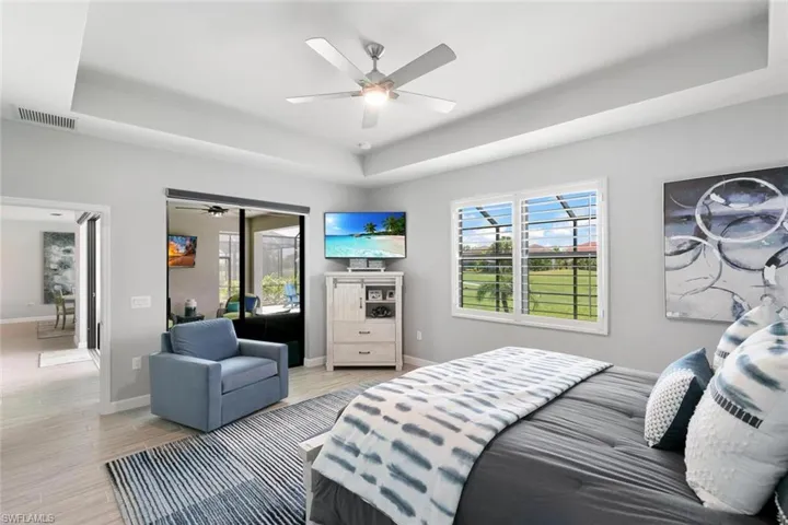 Bedroom featuring light wood-type flooring, a tray ceiling, ceiling fan, and access to exterior