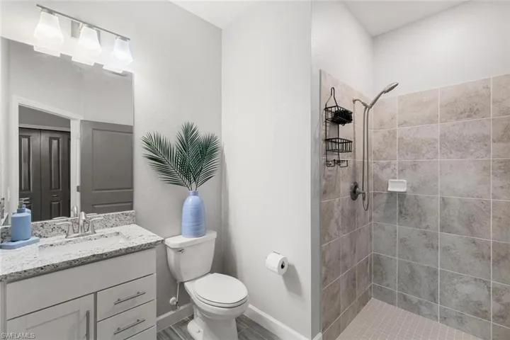Bathroom featuring a tile shower, vanity, and toilet
