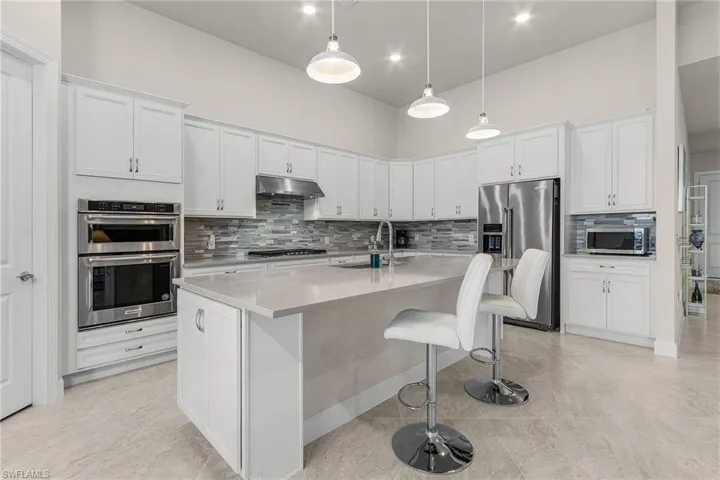Kitchen featuring an island with sink, hanging light fixtures, sink, white cabinetry, and stainless steel appliances