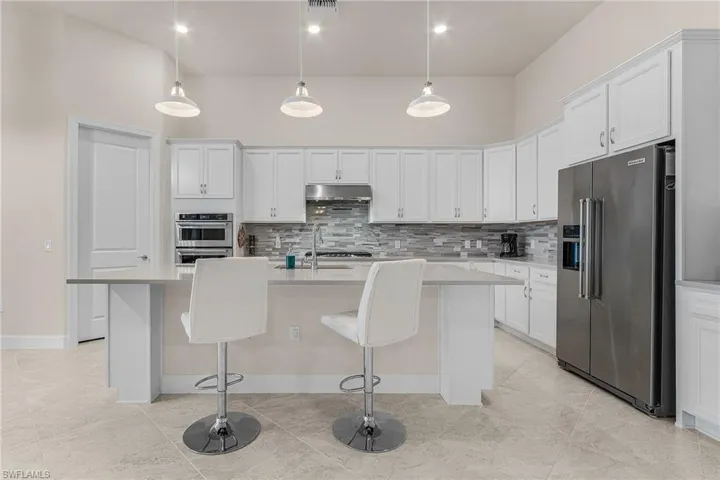 Kitchen featuring appliances with stainless steel finishes, white cabinetry, pendant lighting, and an island with sink