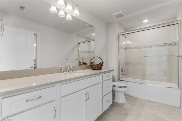 Full bathroom featuring shower / bath combination with glass door, vanity, tile patterned flooring, and toilet
