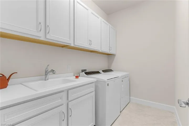 Washroom with cabinets, washing machine and clothes dryer, light tile patterned floors, and sink