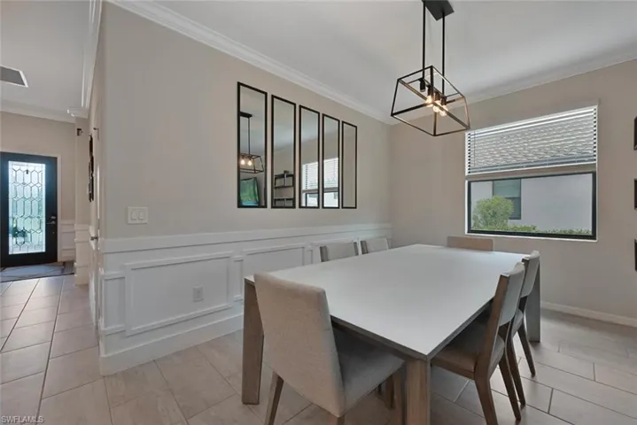 Dining area featuring crown molding, a chandelier, plenty of natural light, wainscoting, and light tile patterned flooring