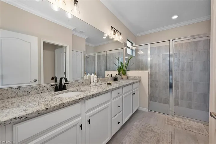 Bathroom featuring double vanity, a stall shower, and ornamental molding