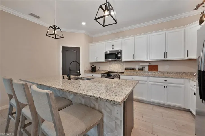 Kitchen with stainless steel appliances, white cabinetry, an island with sink, light stone countertops, and ornamental molding