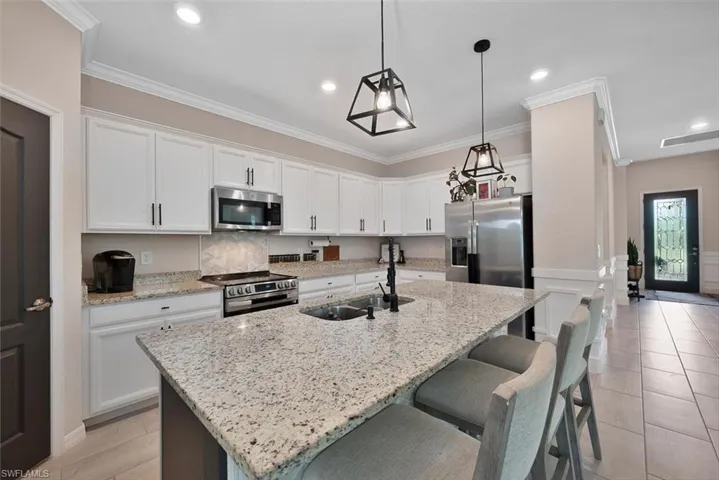 Kitchen featuring appliances with stainless steel finishes, white cabinetry, a center island with sink, a kitchen bar, and light stone countertops