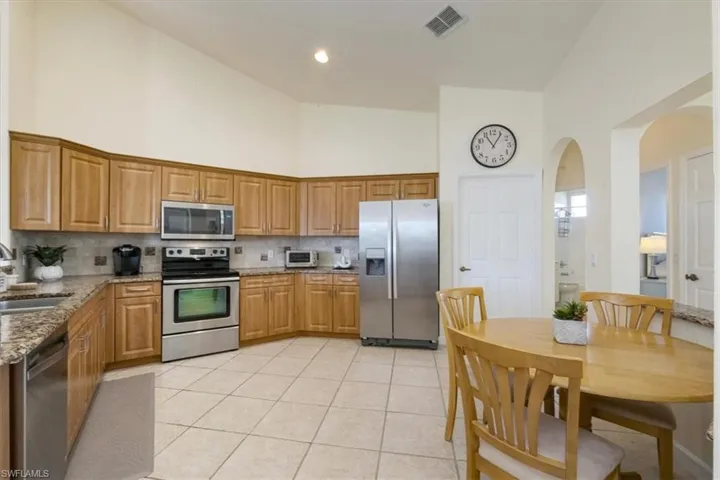 Kitchen featuring high vaulted ceiling, stainless steel appliances, light stone countertops, arched walkways, and decorative backsplash