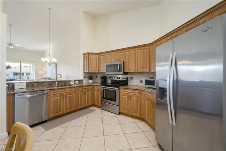 Kitchen with appliances with stainless steel finishes, hanging light fixtures, dark stone counters, a chandelier, and a high ceiling