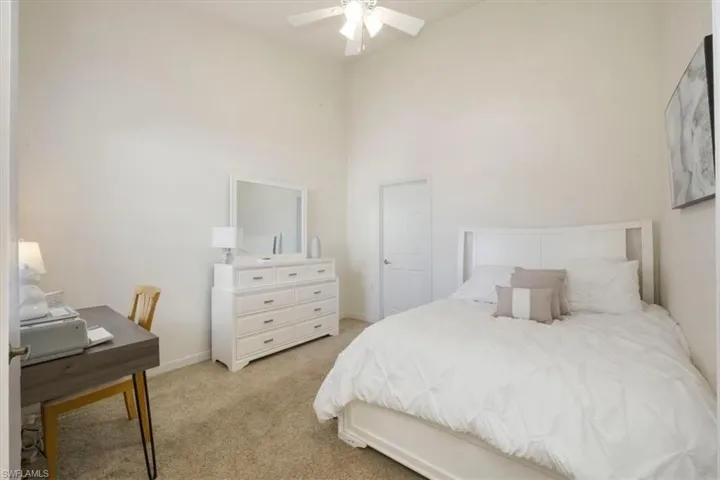 Bedroom featuring light carpet, an office area, ceiling fan, and a high ceiling