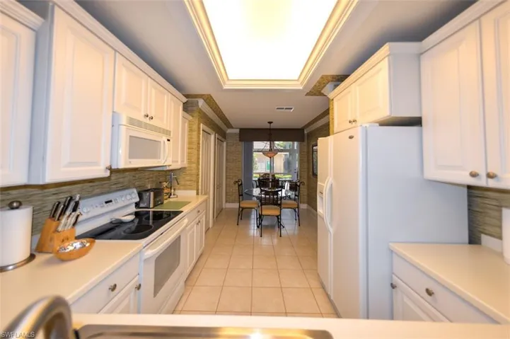 Kitchen featuring light tile patterned flooring, decorative light fixtures, white cabinetry, white appliances, and tasteful backsplash