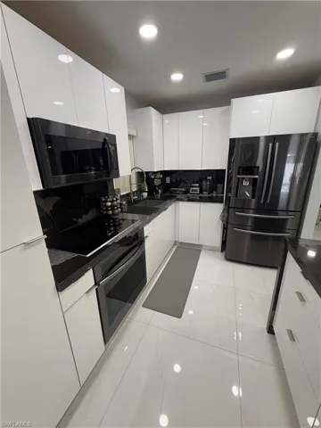 Kitchen with modern cabinets, white cabinetry, black appliances, light marble finish flooring, and backsplash