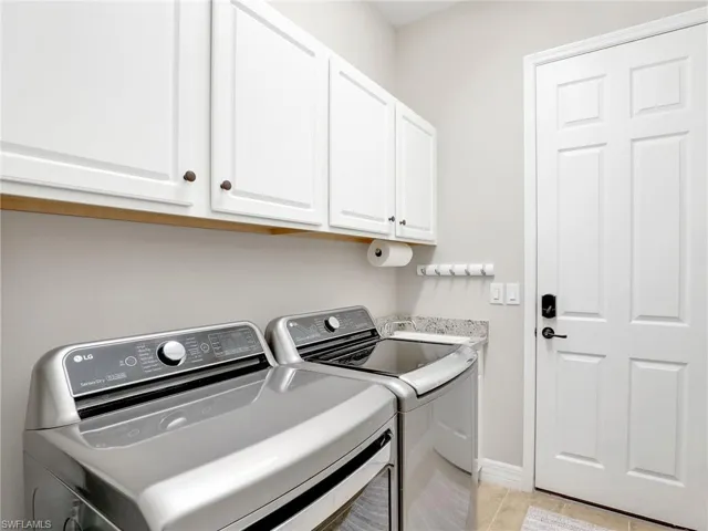 Laundry room with washer and clothes dryer, light tile patterned flooring, and cabinets