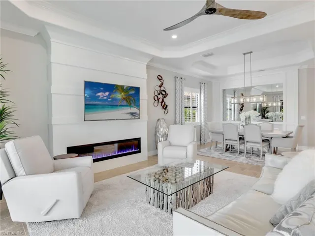 Tiled living room with crown molding, a fireplace, a tray ceiling, and ceiling fan