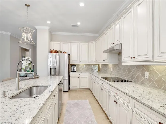 Kitchen featuring light stone countertops, sink, pendant lighting, and white cabinets