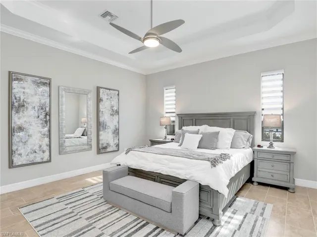 Bedroom with ceiling fan, light tile patterned flooring, ornamental molding, and a tray ceiling