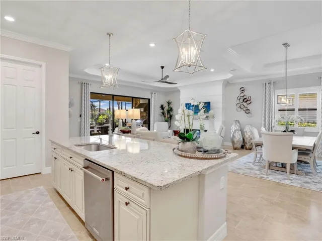 Kitchen with an island with sink, light stone countertops, stainless steel dishwasher, pendant lighting, and sink