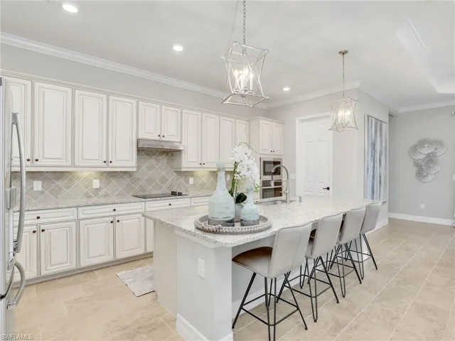 Kitchen featuring a center island with sink, white cabinets, decorative light fixtures, and stainless steel appliances