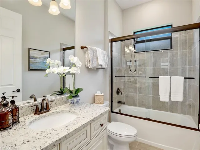 Full bathroom with vanity, toilet, tile patterned floors, and bath / shower combo with glass door