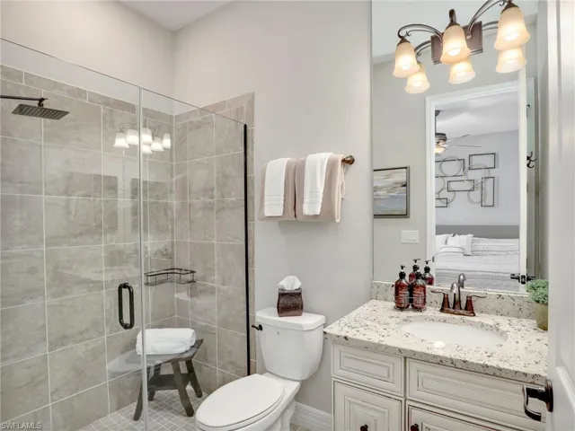 Bathroom featuring vanity, a shower with shower door, toilet, and ceiling fan