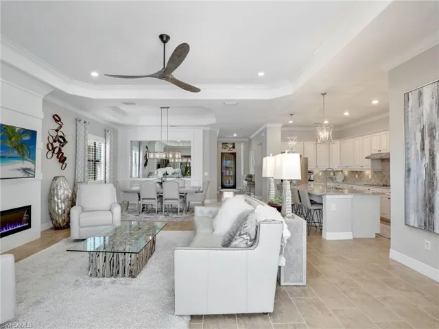 Living room with ornamental molding, a tray ceiling, and ceiling fan with notable chandelier