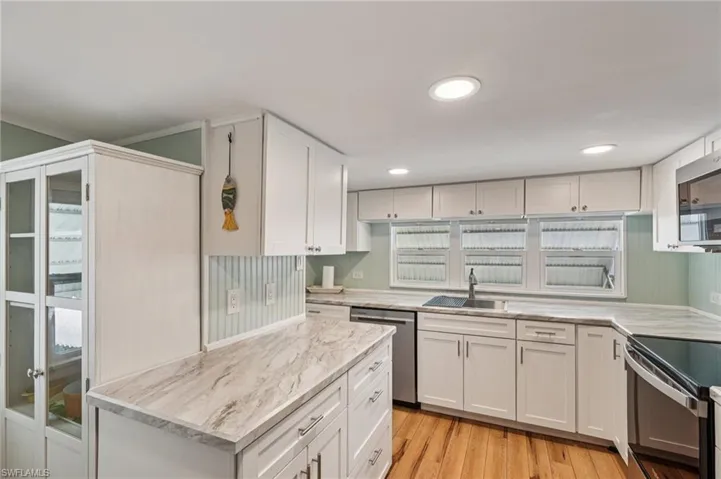 Kitchen featuring stainless steel dishwasher, electric range, white cabinetry, light wood-style flooring, and light stone counters