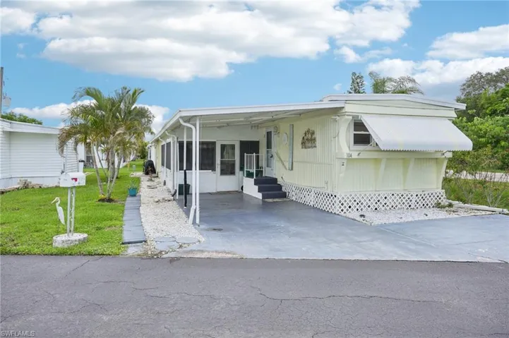 Mobile home featuring entry steps, a front lawn, an attached carport, a sunroom, and driveway