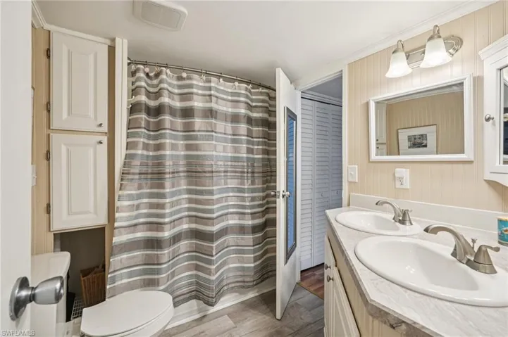 Full bathroom with double vanity, wood finished floors, and a shower with curtain