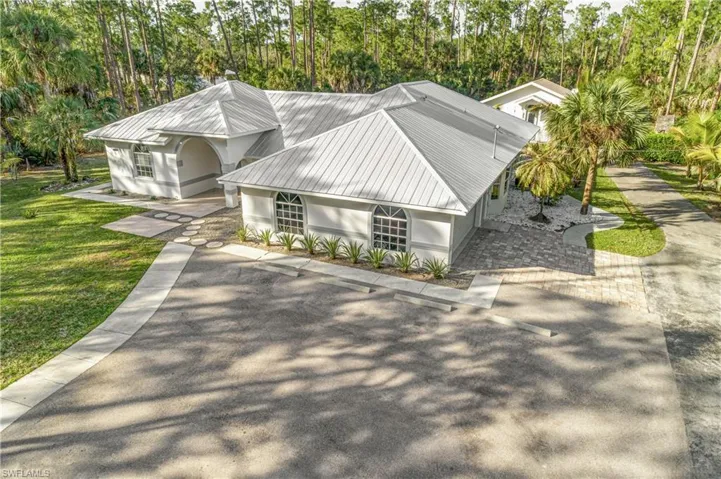 View of home's exterior with a metal roof, a lawn, driveway, and view of scattered trees