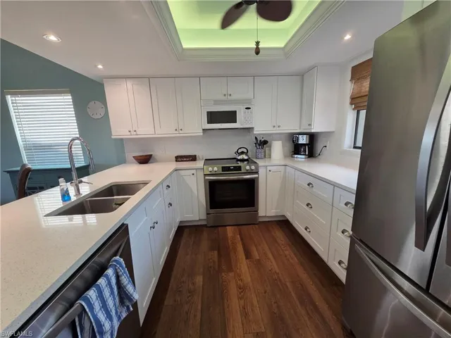 This kitchen features white cabinetry, stainless steel appliances, light-colored countertops, a dual basin sink, and wood-style flooring