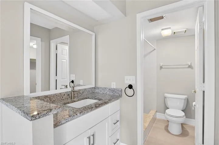 Bathroom vanity with granite countertop, integrated rectangular sink, brushed nickel faucet, and frameless mirror
