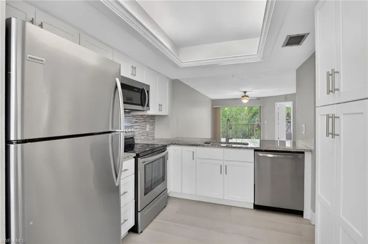 Modern kitchen featuring stainless steel appliances, white shaker cabinetry, and a textured tile backsplash