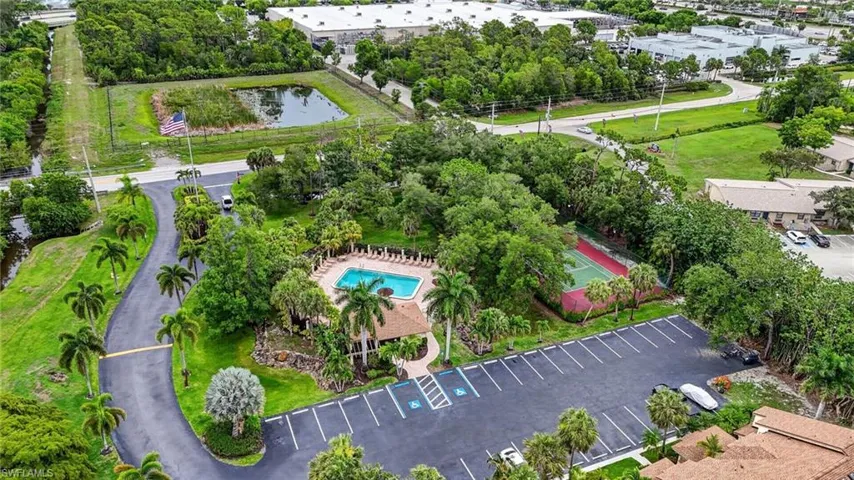 Aerial perspective showcasing a community pool with surrounding lounge chairs, a covered pavilion, and a tennis court