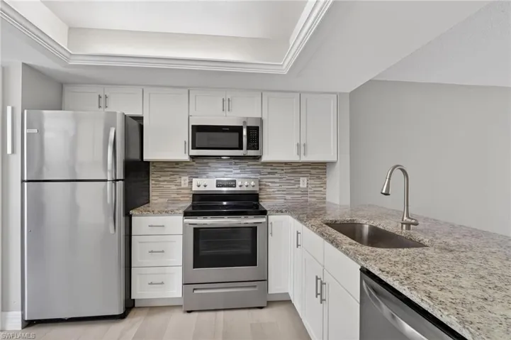 Kitchen featuring white cabinetry, stainless steel appliances, granite countertops, a mosaic tile backsplash, and light wood-finish flooring