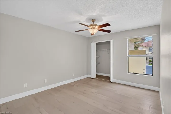 Spacious room featuring wood-finish flooring, light gray walls, and a ceiling fan with integrated lighting