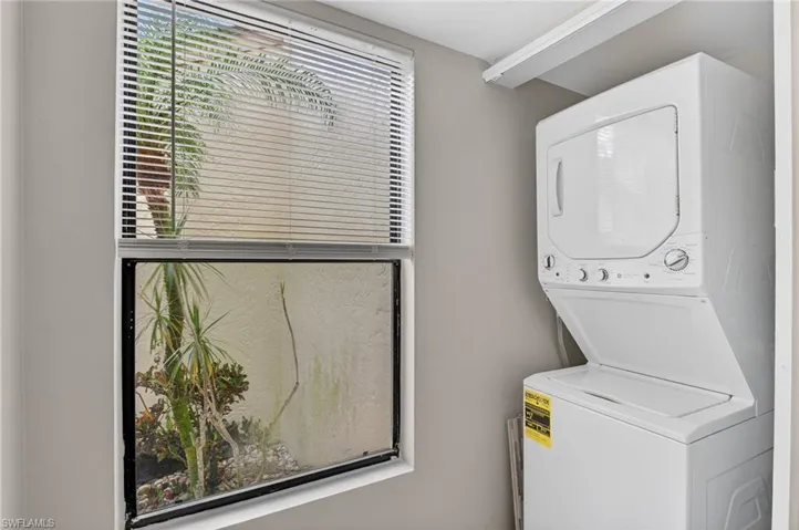 Dedicated laundry area featuring a white stacked washer and dryer unit, neutral wall color, and a window with blinds