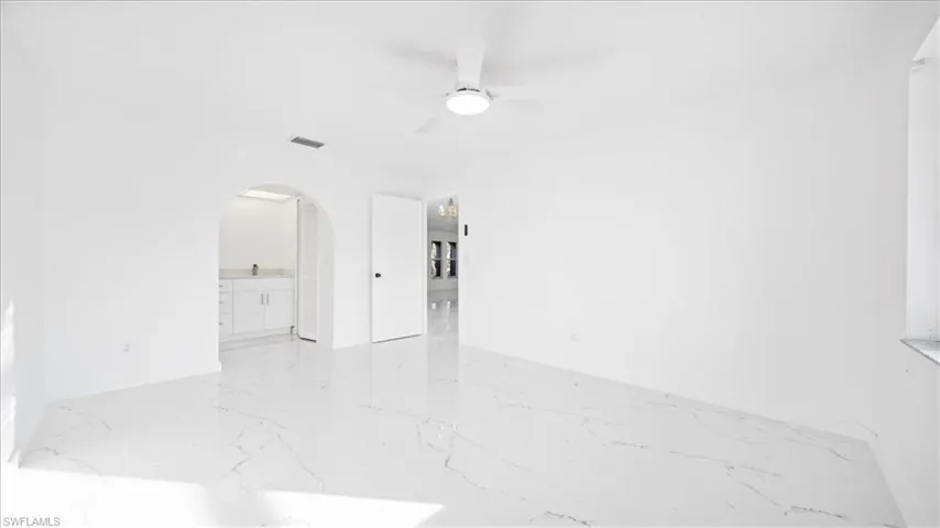 Empty room featuring arched walkways, a ceiling fan, and light marble finish flooring